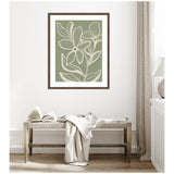 Framed botanical print with white delicate flowers and veins on a muted green background hangs above a rustic wooden bench with a draped light fabric and open book in a bright room.