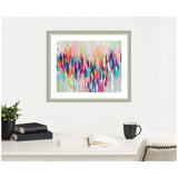 Abstract horizontal brushstroke artwork in bright pinks, blues, and oranges with white dotted accents, framed and displayed above a white desk with books, a plant, and a mug.