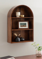 Dark wood arched wall shelf with three compartments holding a white ceramic cup and small bowl, a framed photo, and two black vases with dried grass.