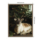 Framed photograph of a reindeer with brown antlers resting under a decorated Christmas tree with red and gold ornaments.