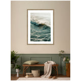 Framed wall art print of an ocean wave cresting under soft morning light above a green paneled wall, with a wooden bench, plants, and cozy textiles below.