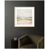 Framed soft pastel landscape depicting a serene beach scene with pale blue sky and beige sandy foreground, hung on a dark gray wall above olive green armchair and small black side table.
