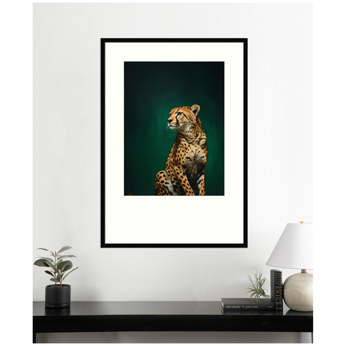 Framed wall art print of a leopard sitting with an emerald green background, mounted above a black console table with a plant, books, and a white lamp.