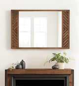 Rectangular wall mirror with a walnut frame featuring diagonal wood slat patterns on the sides, hanging above a mantel decorated with two black vases and a potted green plant.