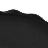 Close-up of a black decorative tray with a scalloped edge and a slightly textured surface under soft lighting