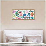 Rectangular framed canvas showing colorful tropical fish and coral in bright blues, pinks, greens, and purples, hung on a beige wall above a white cushioned headboard with neutral pillows.