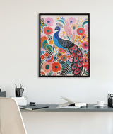 Framed bright colorful boho-style peacock illustration surrounded by pink, red, and orange floral and botanical elements hanging on white wall above minimalist desk with office supplies.