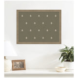 Green botanical block print artwork with small white leaf patterns, framed in light wood, hanging above a white surface with a lamp, photo frame, plant, and bowl.