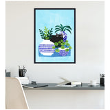 Framed wall art showing a black cat peeking between three potted plants with blue and white patterned pots against a light blue background, hanging above a modern desk.