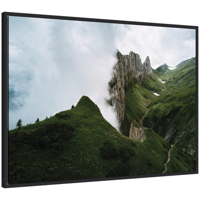 Framed canvas art showing mountain ridge and green meadow on a cloudy day.