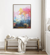 Abstract forest landscape painting with pink, yellow, and blue hues, featuring tall thin trees and a soft, misty effect in a wooden frame hanging above a bench.