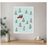 Framed Bex Morley Design print showing snow-covered evergreen trees on pale blue background, with a red car carrying a Christmas tree along winding snowy tracks.