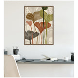 Abstract botanical canvas art with tall, stylized leaves in earthy tones of rust, olive green, brown, and gray, framed in muted wood above a minimalist desk setup.