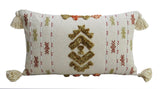 Rectangular cream throw pillow with tassels on all four corners and mustard yellow and rust red embroidered geometric patterns arranged vertically.