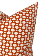 Close-up of Betwixt Pillow Cover in Spark featuring a geometric pattern of small white quatrefoil shapes on a vibrant orange background.