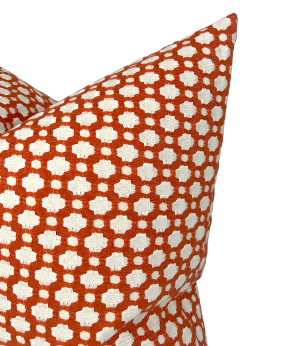 Close-up of Betwixt Pillow Cover in Spark featuring a geometric pattern of small white quatrefoil shapes on a vibrant orange background.