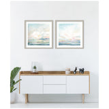 Two framed abstract landscape prints with pastel skies and water reflections in soft blues, pinks, and greens, hung side by side above a modern wood and white sideboard.
