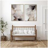 Two framed abstract canvas prints featuring smoky gradients in beige, gray, and black hues hung above a wooden bench with white cushions in a minimalist room.