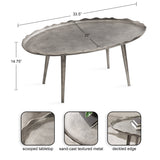 Oval coffee table with a scooped tabletop featuring a deckled edge and sand-cast textured metal surface, standing on four tapered legs, with dimensions overlayed.