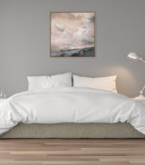 Bedroom with white bedding, beige fabric bed base, gray wall, white bedside lamp, and framed sepia-toned landscape canvas painting of a cloudy sky above hills.