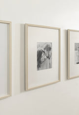 Three cream-colored photo frames with beaded edges, each holding a small black-and-white portrait centered on a white mat, displayed on a white wall in a row.