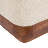 Close-up of a cream-colored textured fabric ottoman corner with a rounded, medium-toned wood base featuring visible grain and smooth finish.