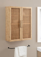 Rectangular wooden wall cabinet with two rattan panel doors and vertical wood handles, mounted over a black towel bar holding a white towel on a beige wall.