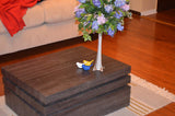 Two small ceramic bird figurines in blue and yellow resting on a dark wooden tiered coffee table with a clear vase of purple flowers.