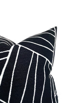 Corner of a black pillow cover featuring a white geometric line pattern creating angular shapes, shown against a white background.