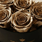Close-up of multiple metallic gold roses arranged tightly in a black round box with gold lettering on the side.