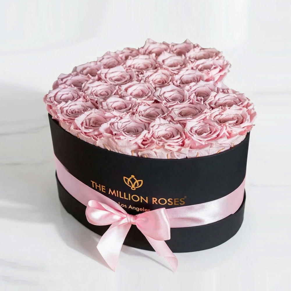 Black heart-shaped box containing 28-30 light pink roses arranged inside