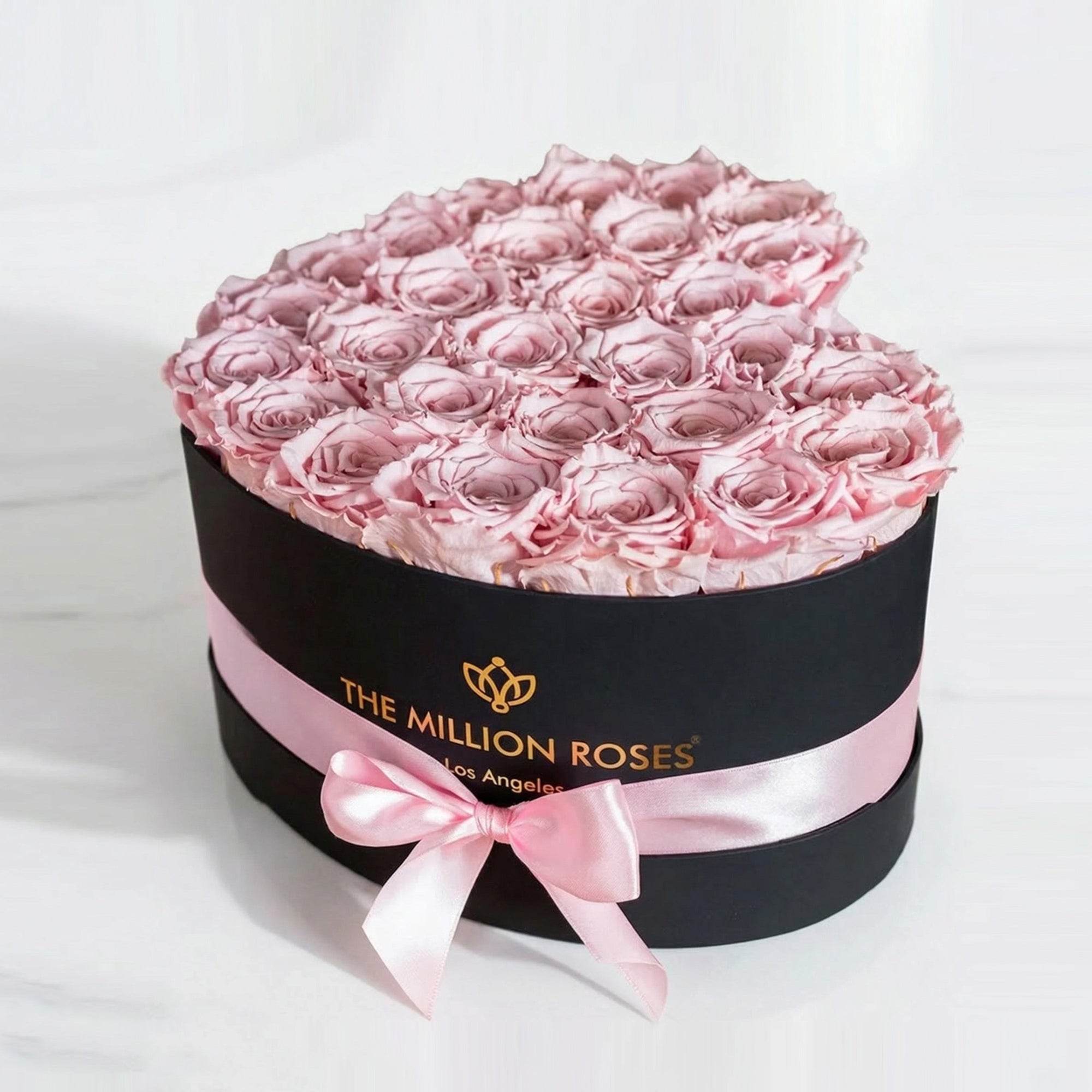 Black heart-shaped box containing 28-30 light pink roses arranged inside