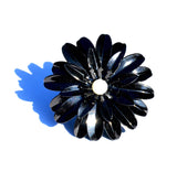 Black floral napkin ring with layered petal design and white center, casting a blue shadow on white background.
