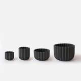 Four black ceramic planters in ascending sizes, each with a vertically ridged wrap design and scalloped rims, arranged side-by-side on a white surface.