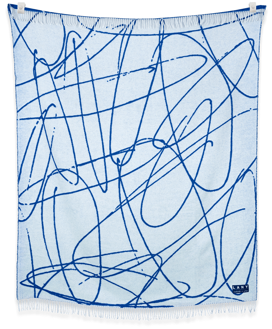 LANY blanket showing hand-drawn design and neutral colors, displayed draped on furniture and hanging