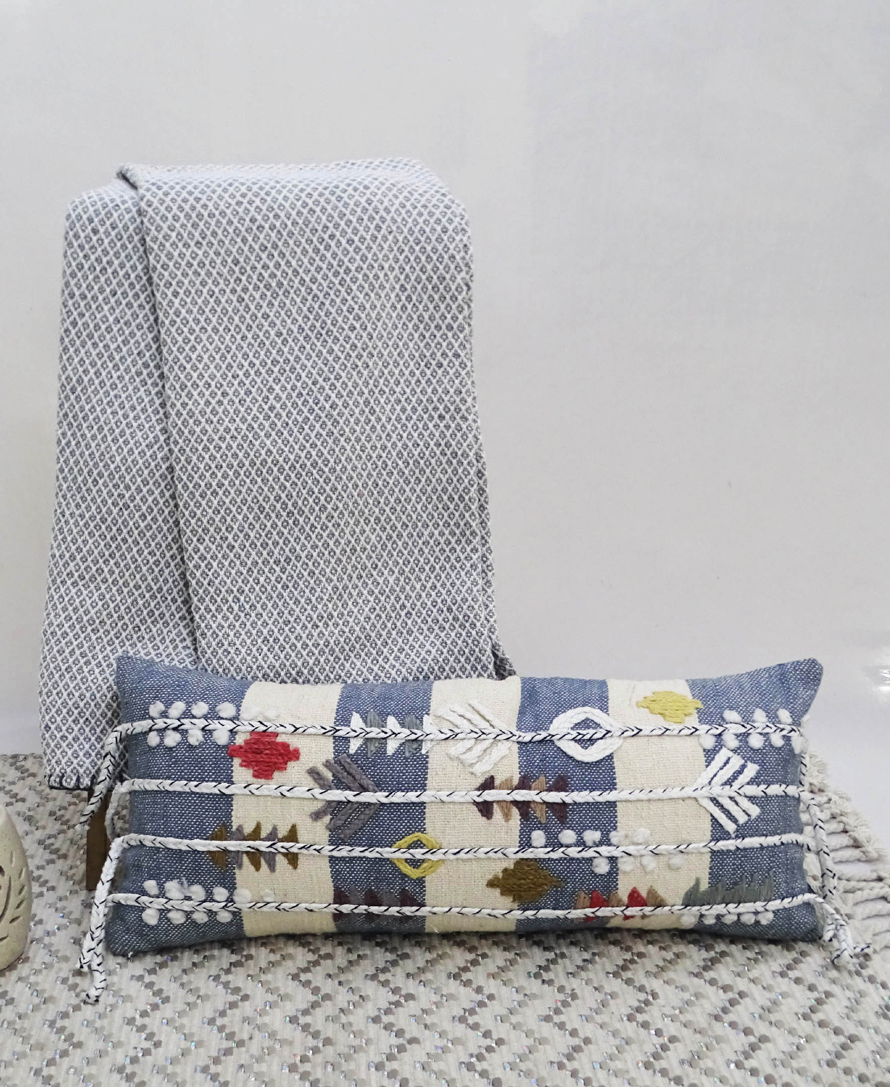 Blue decorative throw pillow with multicolor embroidery and braided detailing on a neutral sofa