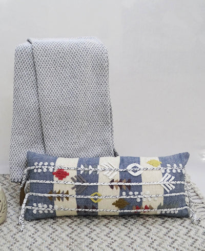 Blue decorative throw pillow with multicolor embroidery and braided detailing on a neutral sofa