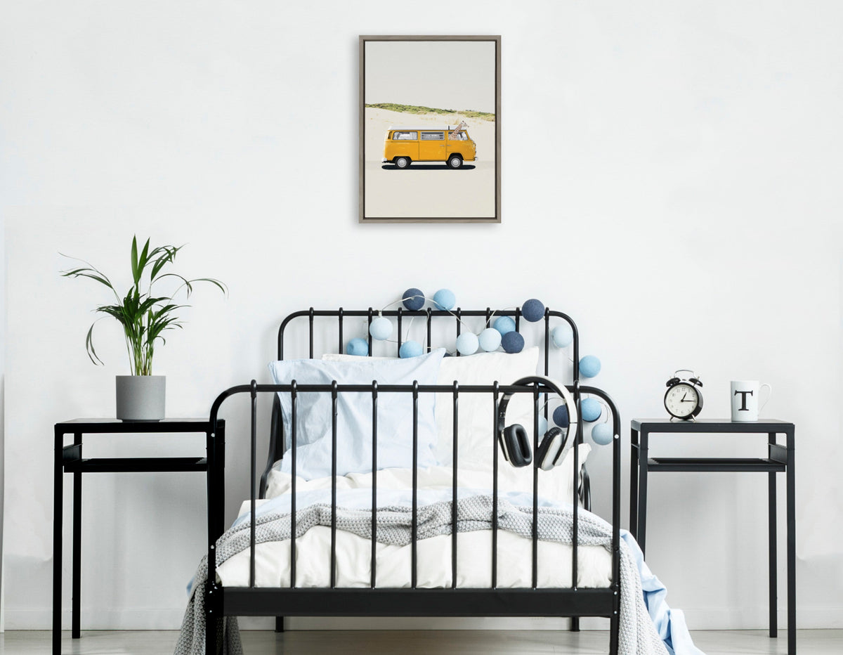 Black metal-framed single bed with white and light blue bedding, flanked by two black side tables holding a plant and a clock, beneath a framed canvas of a yellow van on a desert road.