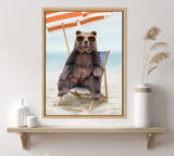 Framed art print of a brown bear wearing orange sunglasses sitting on a blue-striped beach chair under an orange-and-white beach umbrella on sandy shore.