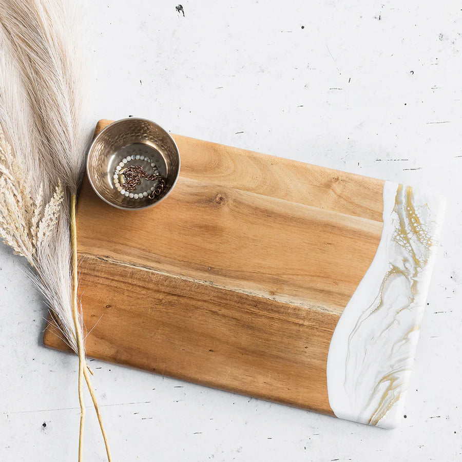 acacia resin serving bread board with marble edge on a white surface with a gold spoon and dried plant.