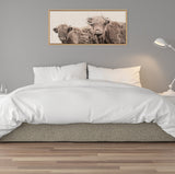 Framed canvas above bed shows two Highland cows with shaggy coats on neutral linen background, highlighting their close, affectionate pose.