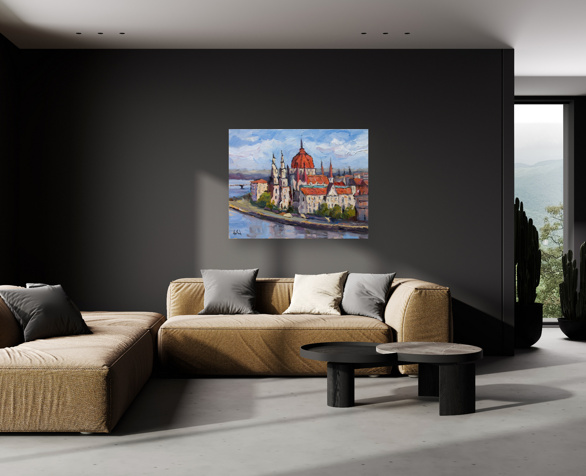 Canvas painting of Budapest featuring red-roofed buildings and a river, mounted on a dark gray wall above a beige sectional sofa with gray and white pillows.