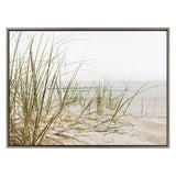 Framed canvas print of beige sand dunes with sparse green beach grass under a soft, pale sky at the coast, offering a serene coastal landscape.