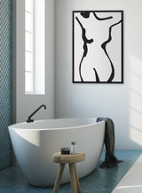 Minimalist bathroom with white freestanding tub, black faucet, small wooden stool holding toiletries, and abstract black-and-white female figure artwork on gray wall.