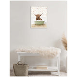 Framed canvas of a brown Highland cow sitting in a pale green clawfoot bathtub against floral wallpaper, hanging above a white bench with a beige fur throw and a taupe bag on a carpeted floor.