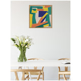 Abstract geometric painting in yellow, green, blue, and orange shapes on neutral linen, framed and hung above a white table with wooden chairs and a vase of white calla lilies.