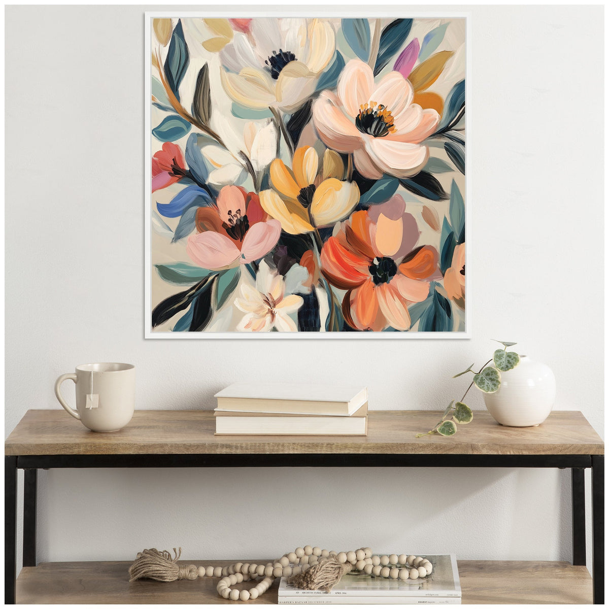 Abstract bouquet painting with large, soft pastel flowers in pink, orange, and cream, accented by deep green and blue leaves in a white frame above a wood and metal console table.