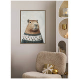 Framed canvas portrait of a capybara wearing a blue and white snowflake sweater, hanging on a beige wall above a textured beige chair with a gold gift and ornament.