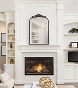 Traditional arched mirror with black ornate metal frame above a white fireplace with burning fire, flanked by built-in shelves and cabinetry in a living room.