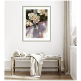 Framed floral painting showing white flowers with orange centers in a glass vase casting soft shadows, hung on a light wall above a wooden bench with a draped cloth and open book.